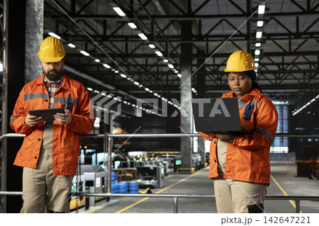 African american woman, supervising factory activity, heavy equipment, industrial space filled with steel work and mechanical systems. Staff overseeing heavy industry engineering operations. 142647221