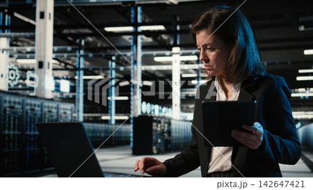 Data center female admin uses devices and AR simulation to conduct security audit on equipment rigs. Woman in server farm uses digital twin scan virtualization to verify firewall protection 142647421