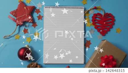Vertical video: Fairy lights turning on, spiral notepad awaiting holiday gift list on cyan paper 142648315