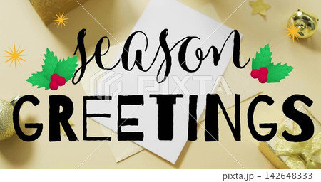 Showing white card and envelope with black season GREETINGS text on beige tabletop, gold bauble 142648333