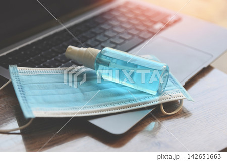 Disinfects the surface of the laptop by sanitizer spray or alcohol gel washing hand hygiene and face mask on the working place for quarantine coronavirus covid-19 working from home concept. Disinfects the surface of the laptop by sanitizer spray or alcohol gel washing hand hygiene and face mask on the working place for quarantine coronavirus covid-19 working from home concept. 142651663