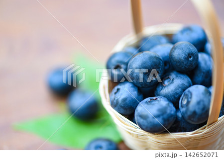 Fresh blueberries fruit in basket and green leaves on wooden background 142652071