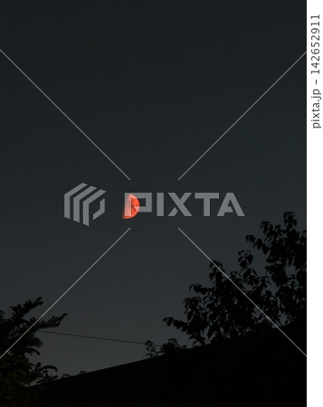 暗闇の夜空に幻想的に輝く赤い半月とシルエット 142652911