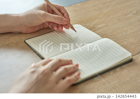ノートに書き込む女性の手元 142654443