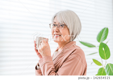 飲み物を手に笑顔を見せるシニア女性。自分時間を楽しむ健康的で豊かな老後のイメージ 飲み物を手に笑顔を見せるシニア女性。自分時間を楽しむ健康的で豊かな老後のイメージ 142654515