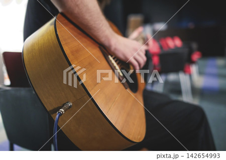 Concert view of acoustic electric guitar player with vocalist and rock band performing in a club, male musician guitarist on stage with audience in a crowded concert club hall arena, hands on guitar Concert view of acoustic electric guitar player with vocalist and rock band performing in a club, male musician guitarist on stage with audience in a crowded concert club hall arena, hands on guitar 142654993