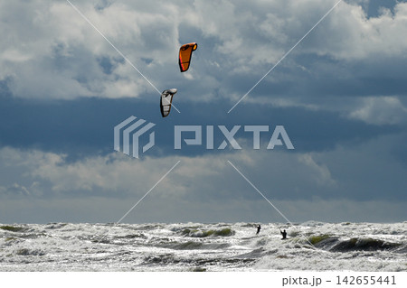 Two Kitesurfers Riding Rough Baltic Sea Waves Under Dramatic Storm Clouds on Windy Day Two Kitesurfers Riding Rough Baltic Sea Waves Under Dramatic Storm Clouds on Windy Day 142655441