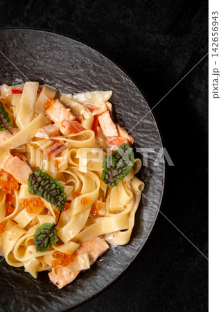 Fish penne. Tasty recipe. Spaghetti with salmon pieces ikura roe small chard leaves coated in creamy sauce on plate isolated on black. 142656943