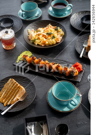 Dinner table. Restaurant set. Asian italian cuisine with alcohol cocktail glass dessert cake piece with hot drink cups served on black. Dinner table. Restaurant set. Asian italian cuisine with alcohol cocktail glass dessert cake piece with hot drink cups served on black. 142656944