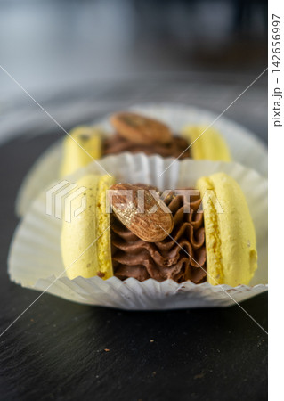Macaron shells. Chocolate ganache. Yellow french baked dessert served in paper liners. Small sugar cookie discs garnished with almond. Macaron shells. Chocolate ganache. Yellow french baked dessert served in paper liners. Small sugar cookie discs garnished with almond. 142656997