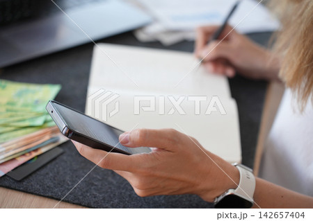Woman checking household expenses with smartphone and notebook Woman checking household expenses with smartphone and notebook 142657404