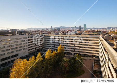Aerial view modern residential district with landscaped courtyard trees, midrise buildings, clear blue sky, autumn foliage and distant urban skyline during daylight Aerial view modern residential district with landscaped courtyard trees, midrise buildings, clear blue sky, autumn foliage and distant urban skyline during daylight 142657660