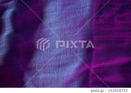 A piece of fabric lies on a surface as light catches its texture. The colors blend from purple to blue A piece of fabric lies on a surface as light catches its texture. The colors blend from purple to blue 142658743
