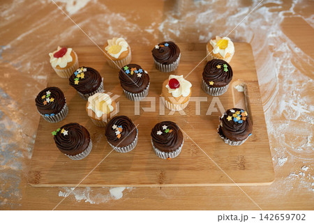 Cupcake, icing and sprinkles on wooden board for eating, birthday party and lunch in house. Muffins, cake and chocolate or vanilla flavor snack for desert, pastry or bakery display with sugar candy Cupcake, icing and sprinkles on wooden board for eating, birthday party and lunch in house. Muffins, cake and chocolate or vanilla flavor snack for desert, pastry or bakery display with sugar candy 142659702
