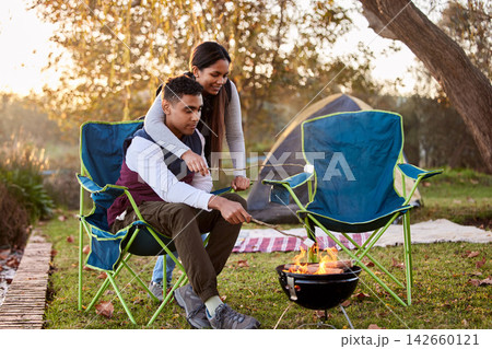 Fire, camping and couple with marshmallows in nature for romantic vacation, adventure or holiday. Love, happy and young man and woman roasting candy by flame on outdoor weekend trip together. 142660121