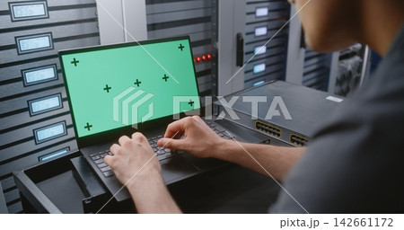 Male IT Engineer Using Laptop with Green Screen Near Server Racks in Data Center 142661172