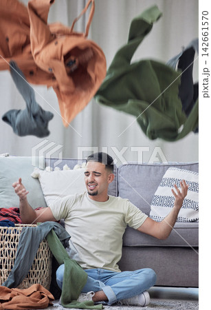 Laundry, frustrated and man on floor for spring cleaning, burnout and chaos with clothes in air. Stress, overworked and angry in apartment for fatigue, housework and overwhelmed with messy house 142661570