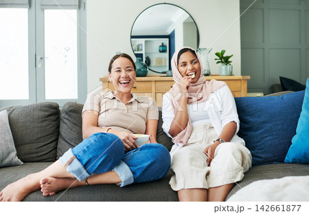 Women friends and eating on sofa with smiling for happy in house for relax with snack. Female people, couch and living room and laugh with islam for diversity with asian with streaming in apartment 142661877