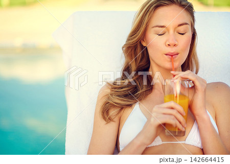 Woman, juice and drink by swimming pool on lounge chair for summer holiday or tropical vacation. Young person or tourist in bikini by hotel with healthy drink, cocktail or alcohol for outdoor break Woman, juice and drink by swimming pool on lounge chair for summer holiday or tropical vacation. Young person or tourist in bikini by hotel with healthy drink, cocktail or alcohol for outdoor break 142664415