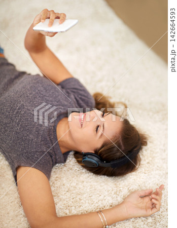 Headphones, smartphone and woman on carpet in home for audio playlist with streaming kpop music and radio. Mobile, listening and gen z girl on floor with podcast for learning language and chat app 142664593