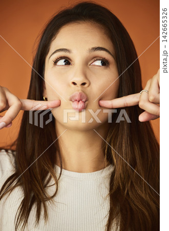 Funny face, fingers and woman in studio for humor, comedy or cheeks dimples on orange background. Female person, lips and playful gen z model for comic emoji, silly facial expression or joking mood Funny face, fingers and woman in studio for humor, comedy or cheeks dimples on orange background. Female person, lips and playful gen z model for comic emoji, silly facial expression or joking mood 142665326