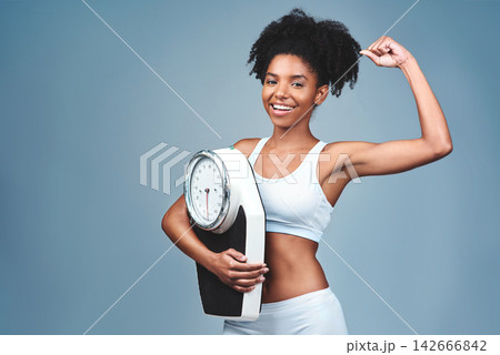 Black girl, portrait and bicep for scale in studio, weight loss and confident measure on blue background. Female person, fitness and diet for balance, mockup space and strong proud for empowerment Black girl, portrait and bicep for scale in studio, weight loss and confident measure on blue background. Female person, fitness and diet for balance, mockup space and strong proud for empowerment 142666842