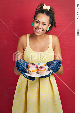 Happy woman, portrait and baker with cupcakes for dessert, food or sweet treat on a red studio background. Young female person with smile or mittens for hot baking or hospitality in yellow dress Happy woman, portrait and baker with cupcakes for dessert, food or sweet treat on a red studio background. Young female person with smile or mittens for hot baking or hospitality in yellow dress 142667976
