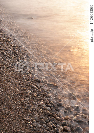 Long exposure vertical shot of gentle sunset wave flowing over pebble beach 142668869