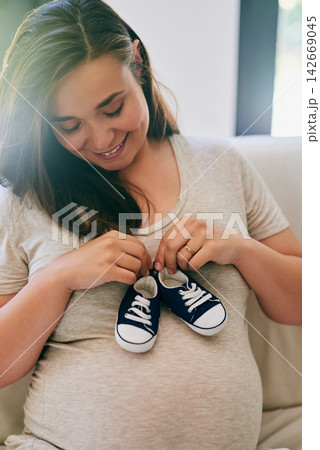 Happy, pregnant woman and shoes on belly in home for reveal of boy gender, journey and experience of pregnancy. Mother to be, holding sneakers and stomach for love or bonding and motherhood with care Happy, pregnant woman and shoes on belly in home for reveal of boy gender, journey and experience of pregnancy. Mother to be, holding sneakers and stomach for love or bonding and motherhood with care 142669045