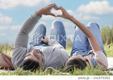 Grass, couple or picnic with heart hands relaxing in park for romantic date, love or celebration together. People, man and woman in nature for bonding, relationship and calm day on weekend outdoor Grass, couple or picnic with heart hands relaxing in park for romantic date, love or celebration together. People, man and woman in nature for bonding, relationship and calm day on weekend outdoor 142670302