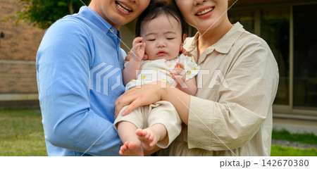 庭で赤ちゃんを優しく抱っこする若い両親の家族写真 142670380