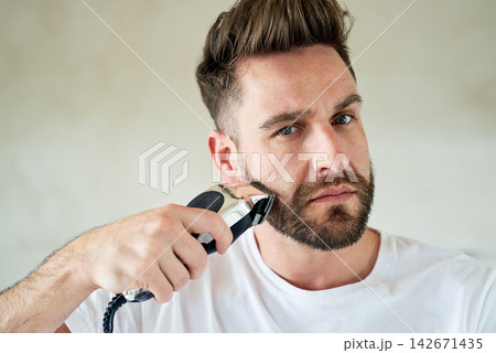 Man, portrait and electric shaver in bathroom for grooming, skincare or morning routine. Face, beard or serious person with trimmer for cleaning, health or hair removal for hygiene in home for beauty 142671435