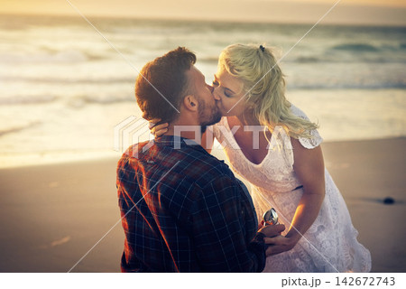 Kiss, engagement and couple with ring on beach for proposal, celebration and anniversary outdoors. Dating, marriage and man and woman with jewellery for honeymoon, vacation and romantic holiday Kiss, engagement and couple with ring on beach for proposal, celebration and anniversary outdoors. Dating, marriage and man and woman with jewellery for honeymoon, vacation and romantic holiday 142672743