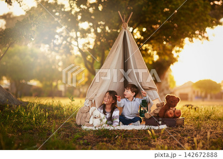 Teepee, kids and fun in garden tent outdoor in nature for camping, playing and adventure with pointing. Cloth, light and fantasy house for children in forest with imagination, suitcase and teddy bear 142672888