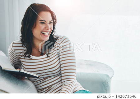 Happy woman, book and laughing on sofa with romance novel, story or literature to relax in home living room. Funny, smile or girl reading fantasy, fiction or mystery on couch in lounge at apartment 142673646