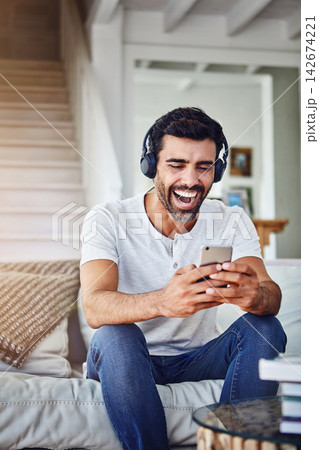 Man, headphones and laughing with phone on sofa for funny video, social media post and comedy movie on mobile app. Person, smartphone and happy for listening to audio, sound and subscription in home Man, headphones and laughing with phone on sofa for funny video, social media post and comedy movie on mobile app. Person, smartphone and happy for listening to audio, sound and subscription in home 142674221
