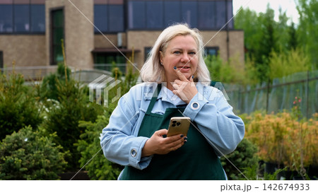 Portrait of happy female gardener standing among bright greenery of her garden 142674933