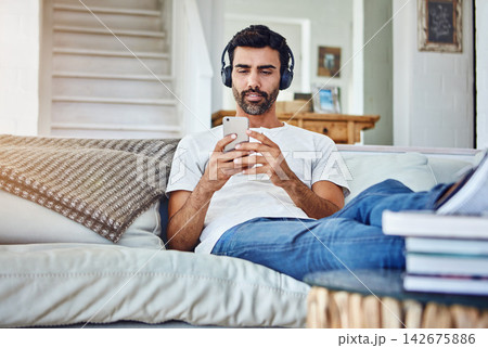 Man, phone and video with headphones on sofa for sound, audio and streaming service in living room with relax. Person, smartphone and mobile app for listening to music, radio and subscription in home Man, phone and video with headphones on sofa for sound, audio and streaming service in living room with relax. Person, smartphone and mobile app for listening to music, radio and subscription in home 142675886