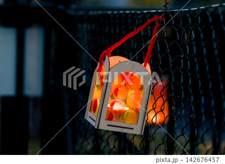 Decorative Autumn Lantern Hanging on Wire Fence with Glowing Candlelight at Dusk Decorative Autumn Lantern Hanging on Wire Fence with Glowing Candlelight at Dusk 142676457