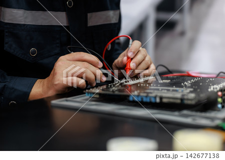 Close-up of an electronics technician using test probes on a circuit board in a repair workshop, checking computer hardware with focused hands. Close-up of an electronics technician using test probes on a circuit board in a repair workshop, checking computer hardware with focused hands. 142677138