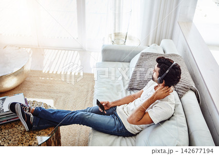 Man, phone and relax with headphones in home for music, radio or streaming podcast in living room with top view. Person, smartphone or mobile app for listening to audio, sound or subscription on sofa Man, phone and relax with headphones in home for music, radio or streaming podcast in living room with top view. Person, smartphone or mobile app for listening to audio, sound or subscription on sofa 142677194