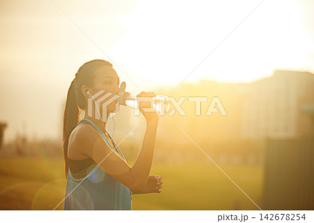 Woman, runner and drinking water with earphones for exercise with audio, subscription or detox in city. Girl, person and athlete at training, workout or sound for music streaming with health on road Woman, runner and drinking water with earphones for exercise with audio, subscription or detox in city. Girl, person and athlete at training, workout or sound for music streaming with health on road 142678254
