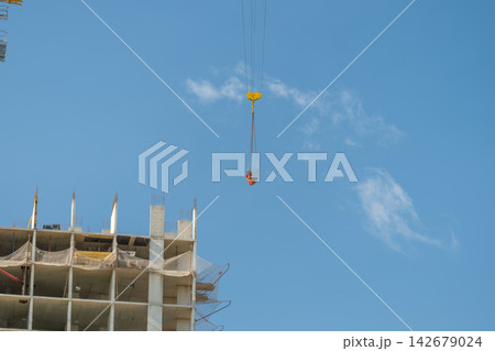 Construction crane lifting materials high above a building site under a clear blue sky filled with wispy clouds Construction crane lifting materials high above a building site under a clear blue sky filled with wispy clouds 142679024
