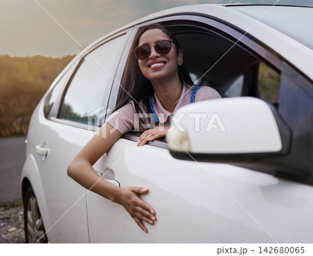Woman, adventure and happy in car window with smile for travel or road trip with relaxing journey in summer. Weekend, holiday and stress relief with vacation or ride in countryside for view with calm Woman, adventure and happy in car window with smile for travel or road trip with relaxing journey in summer. Weekend, holiday and stress relief with vacation or ride in countryside for view with calm 142680065
