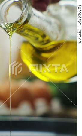 Vertical video. Woman pours oil on a frying pan on an electric stove. Modern kitchen appliance. Food preparation - pouring oil on frying pan. 142680288