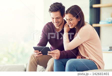 Happy, couple and relax with tablet in in living room for social media, news or streaming video together. Digital technology, man and woman on sofa for online shopping or reading blog on app in home 142681401