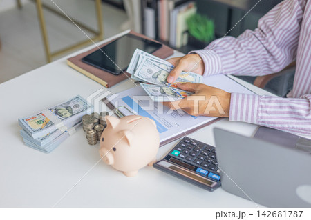 Businessman counting cash and organizing finances with money and piggy bank on the table. Businessman counting cash and organizing finances with money and piggy bank on the table. 142681787