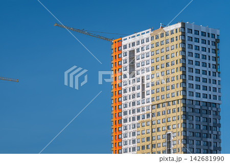 New skyscraper construction rises against a clear blue sky showcasing vibrant colors and modern architecture in a bustling city New skyscraper construction rises against a clear blue sky showcasing vibrant colors and modern architecture in a bustling city 142681990