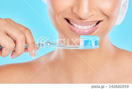 Hands, studio or happy woman brushing teeth with dental toothpaste for healthy oral hygiene. Product, fresh or face of girl cleaning mouth with brush for smile closeup or wellness on blue background Hands, studio or happy woman brushing teeth with dental toothpaste for healthy oral hygiene. Product, fresh or face of girl cleaning mouth with brush for smile closeup or wellness on blue background 142682059