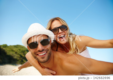 Couple, sunglasses and piggyback on vacation, smile and peace at beach or game by blue sky. People, happy and tropical island for bonding on weekend, outdoor nature and love for marriage or romance 142682696